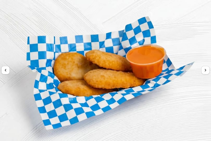 Golden brown chicken nuggets in a blue and white checkered paper boat with a side of orange dipping sauce.